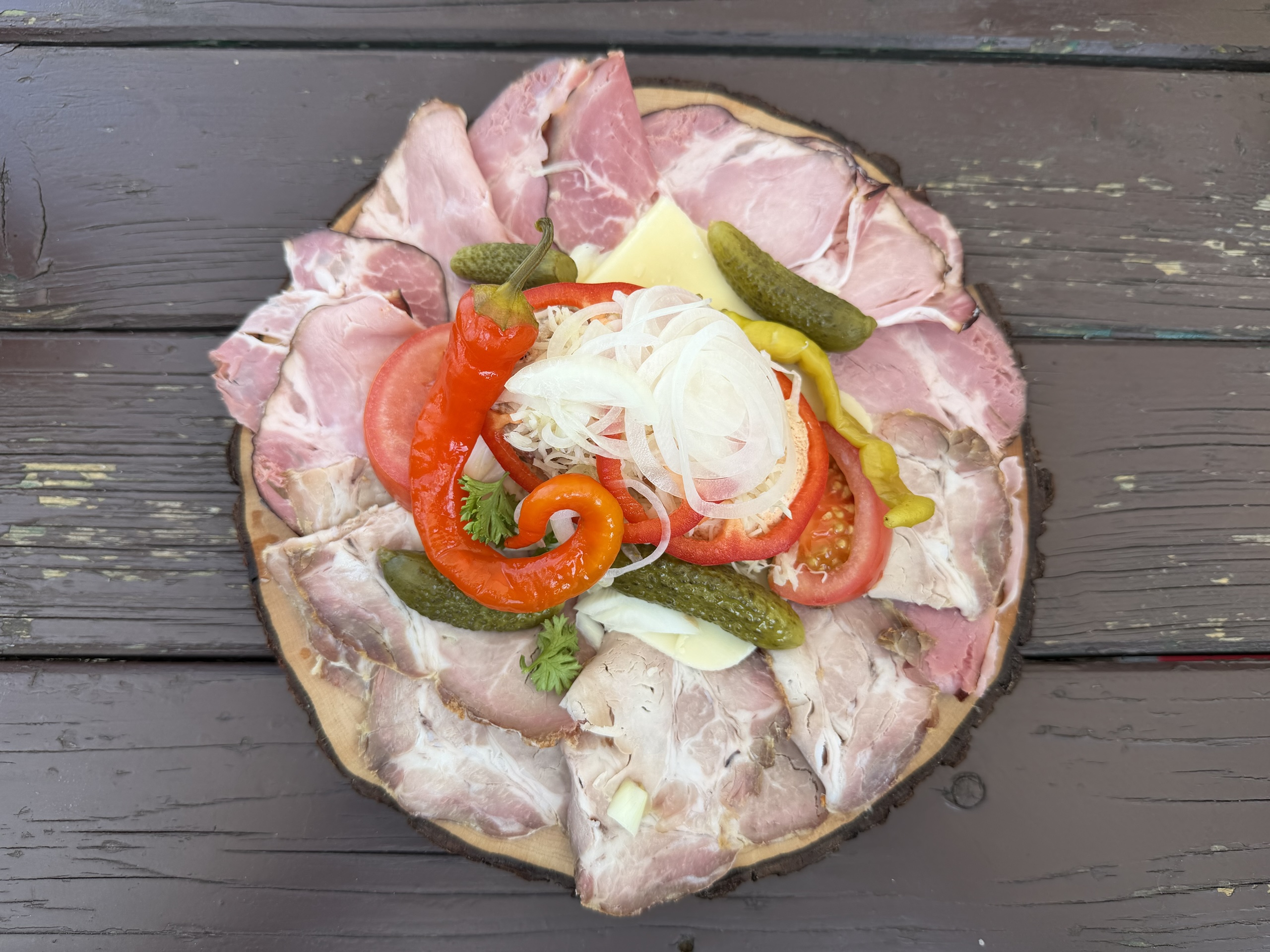 Sliced meats, cheese, pickles, peppers, tomatoes, and onions arranged on a wooden board.