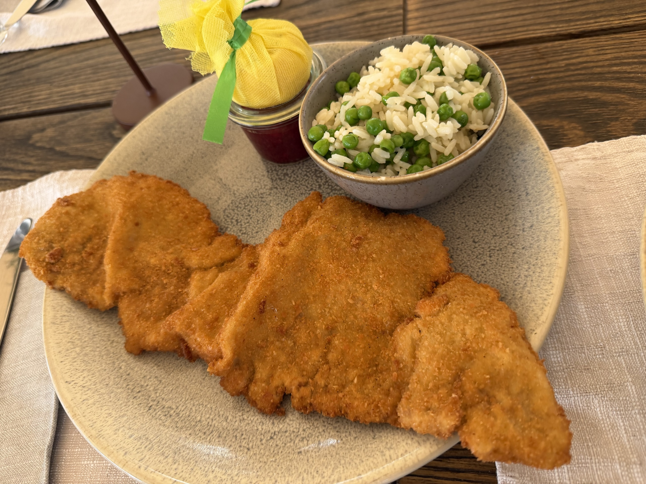 Breaded cutlets on a plate beside a bowl of rice and peas.