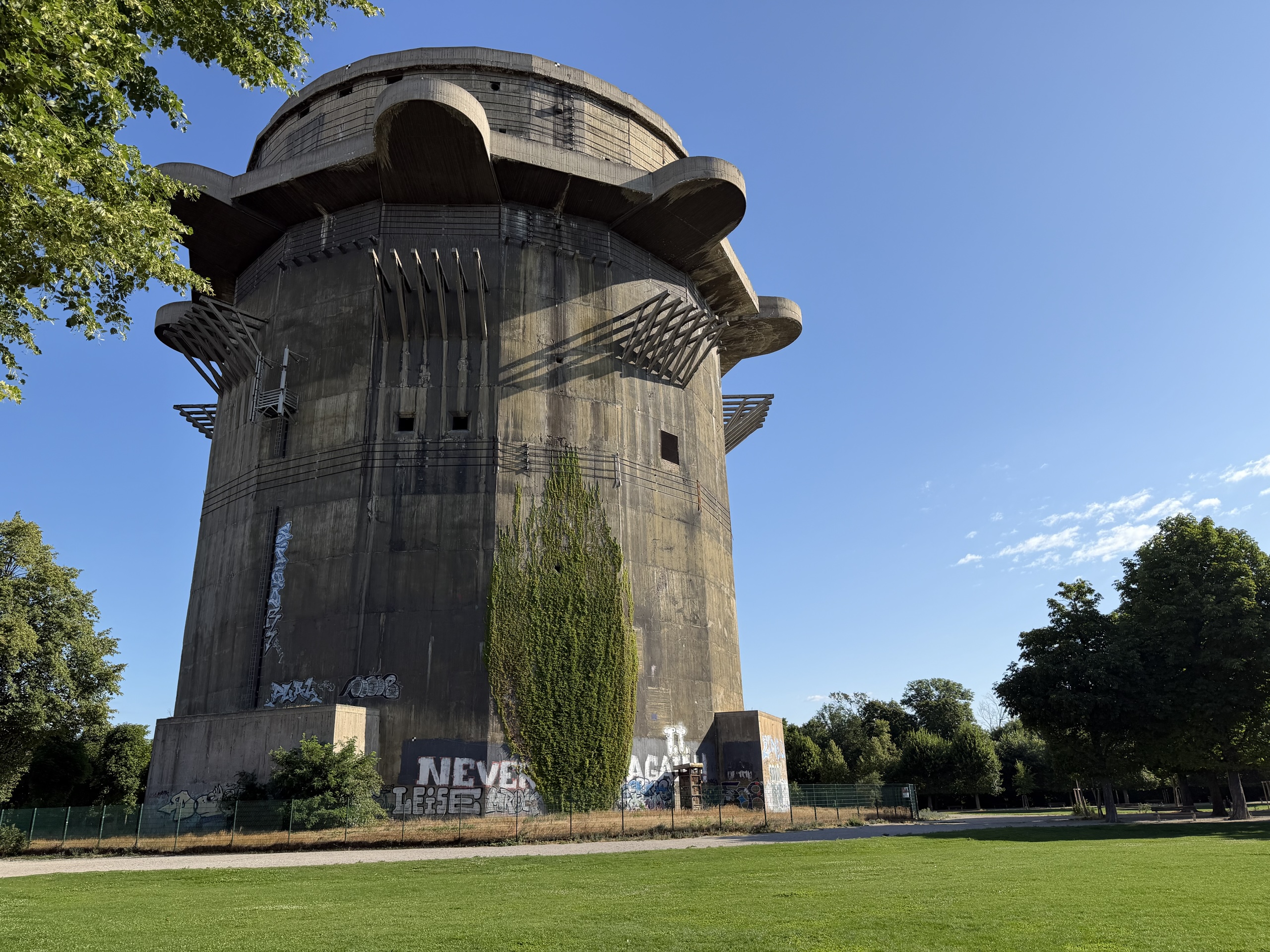 A large cylindrical concrete structure with graffiti and ivy beneath a blue sky.