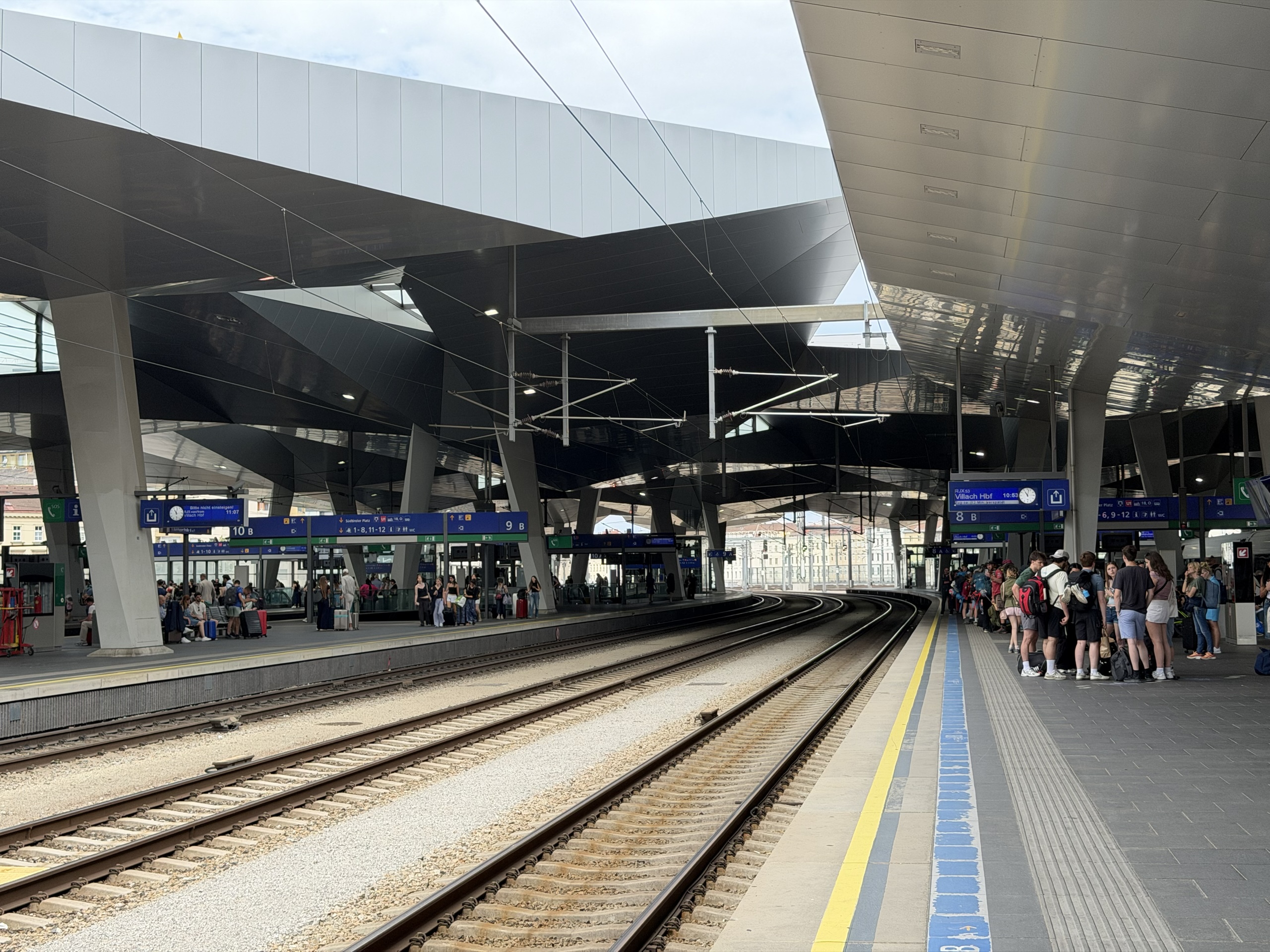 Train tracks curve between crowded platforms beneath a modern station roof.